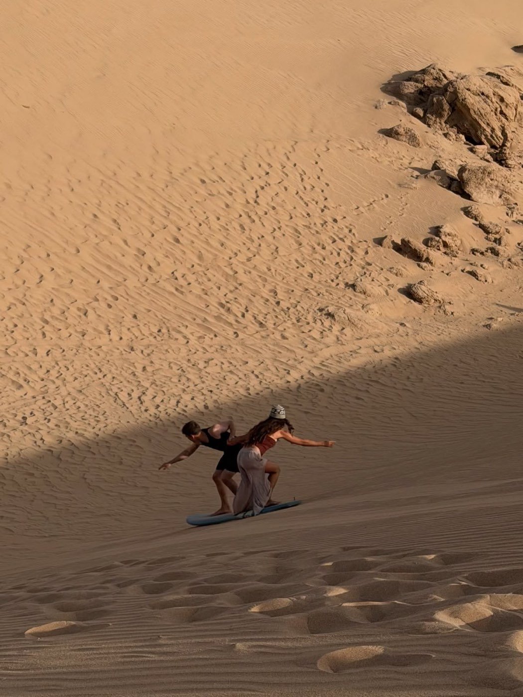 Guía ayudando a un invitado a bajar una duna con la tabla de sandboard