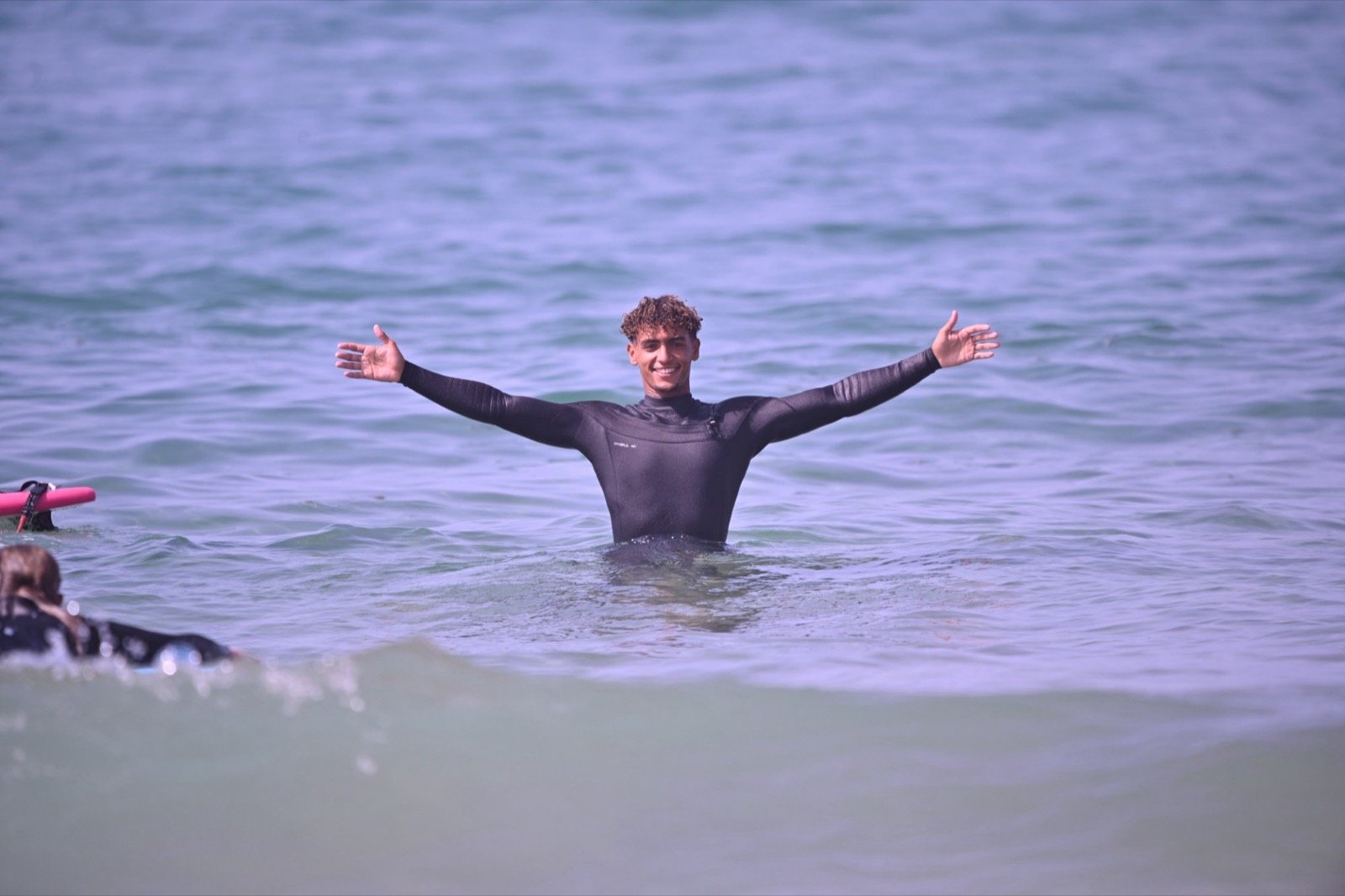 Ismail, instructor de surf de Ayour Surf School, en el agua con los brazos abiertos