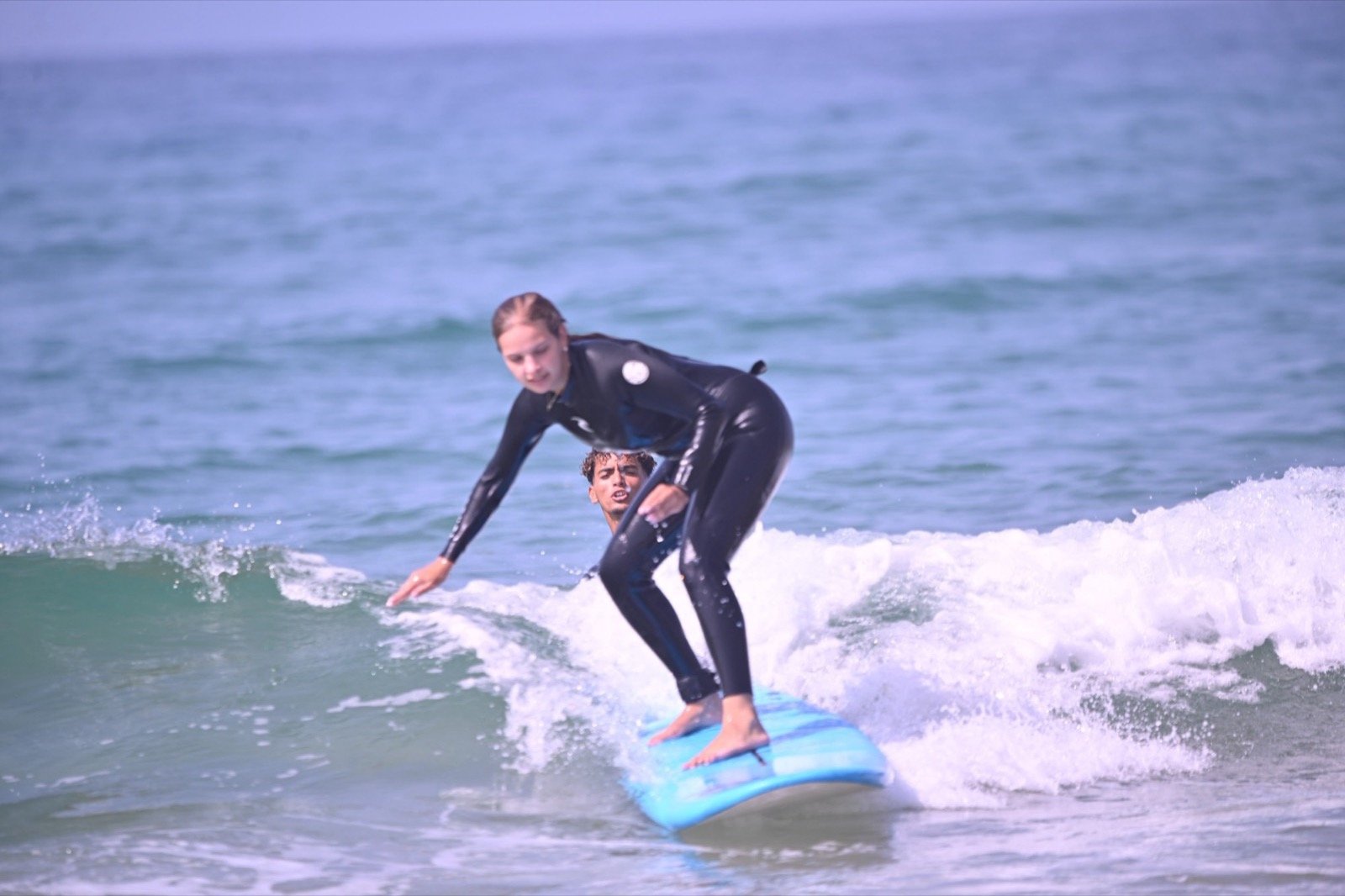Ismail en el agua detrás de un alumno que está surfeando una ola en Taghazout