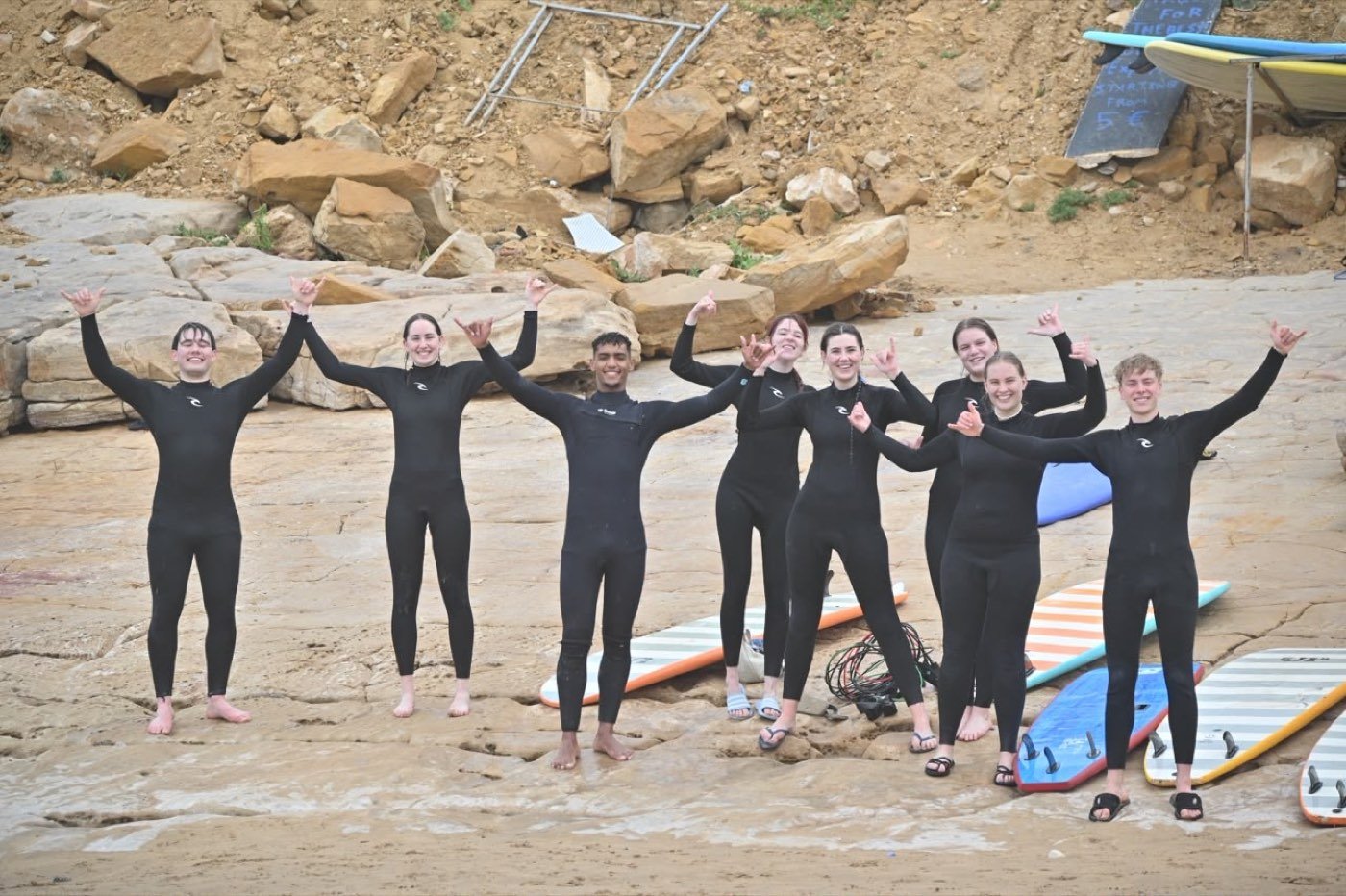 Group of surf students cheering with their arms up next to their boards