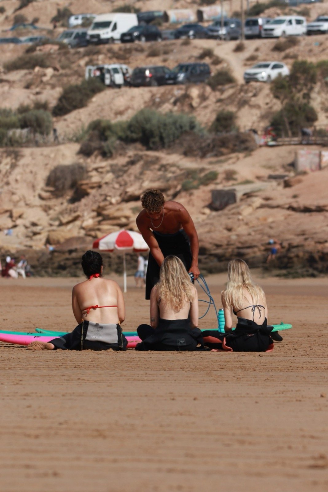 Ismail explicando la clase a un grupo pequeño de alumnos sentados en sus tablas en la playa de Taghazout