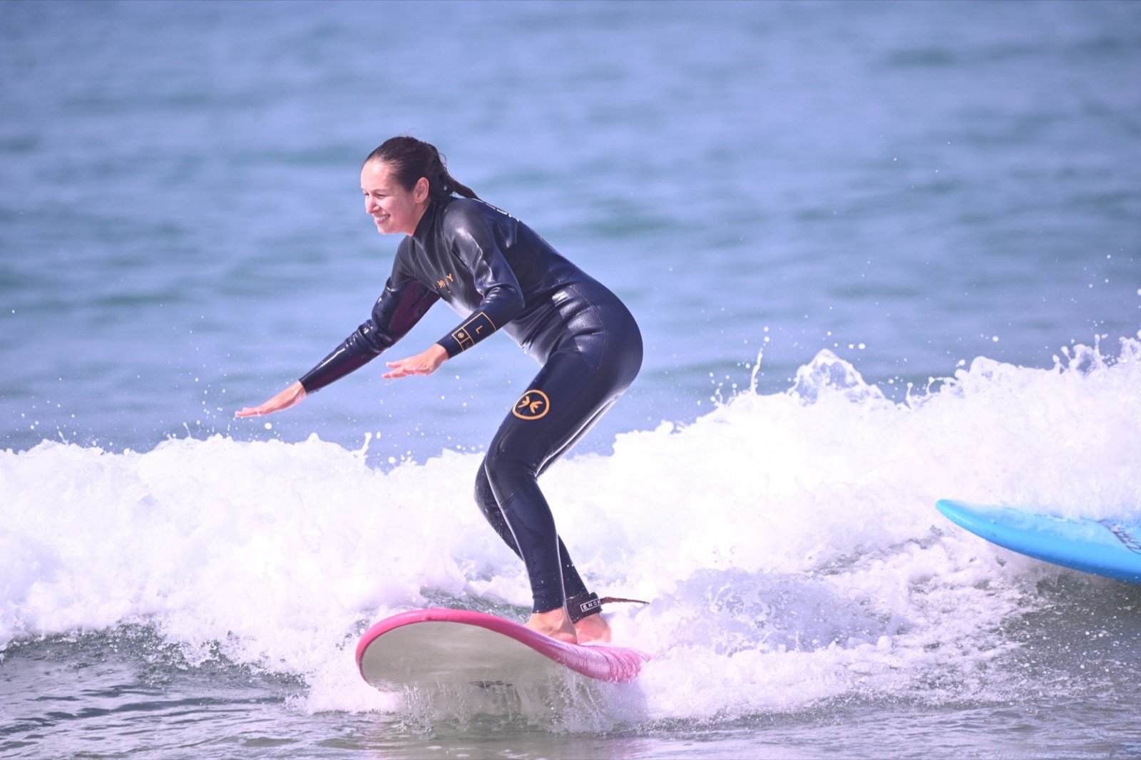 Alumna de surf surfeando una ola sobre una tabla rosa durante una clase en Taghazout