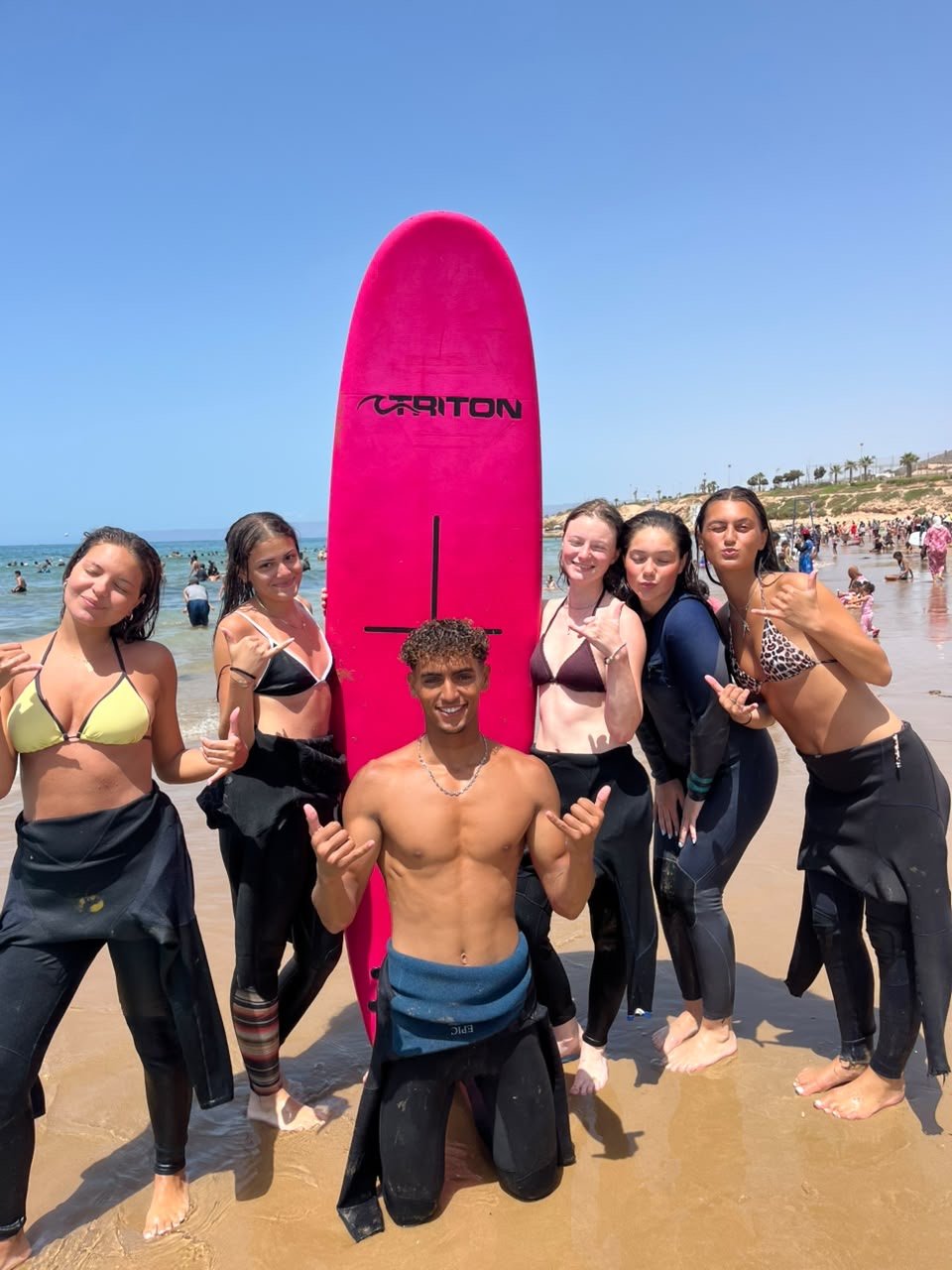 Ismail, instructor de surf de Ayour Surf School, con un grupo de alumnos y una tabla rosa en la playa de Taghazout