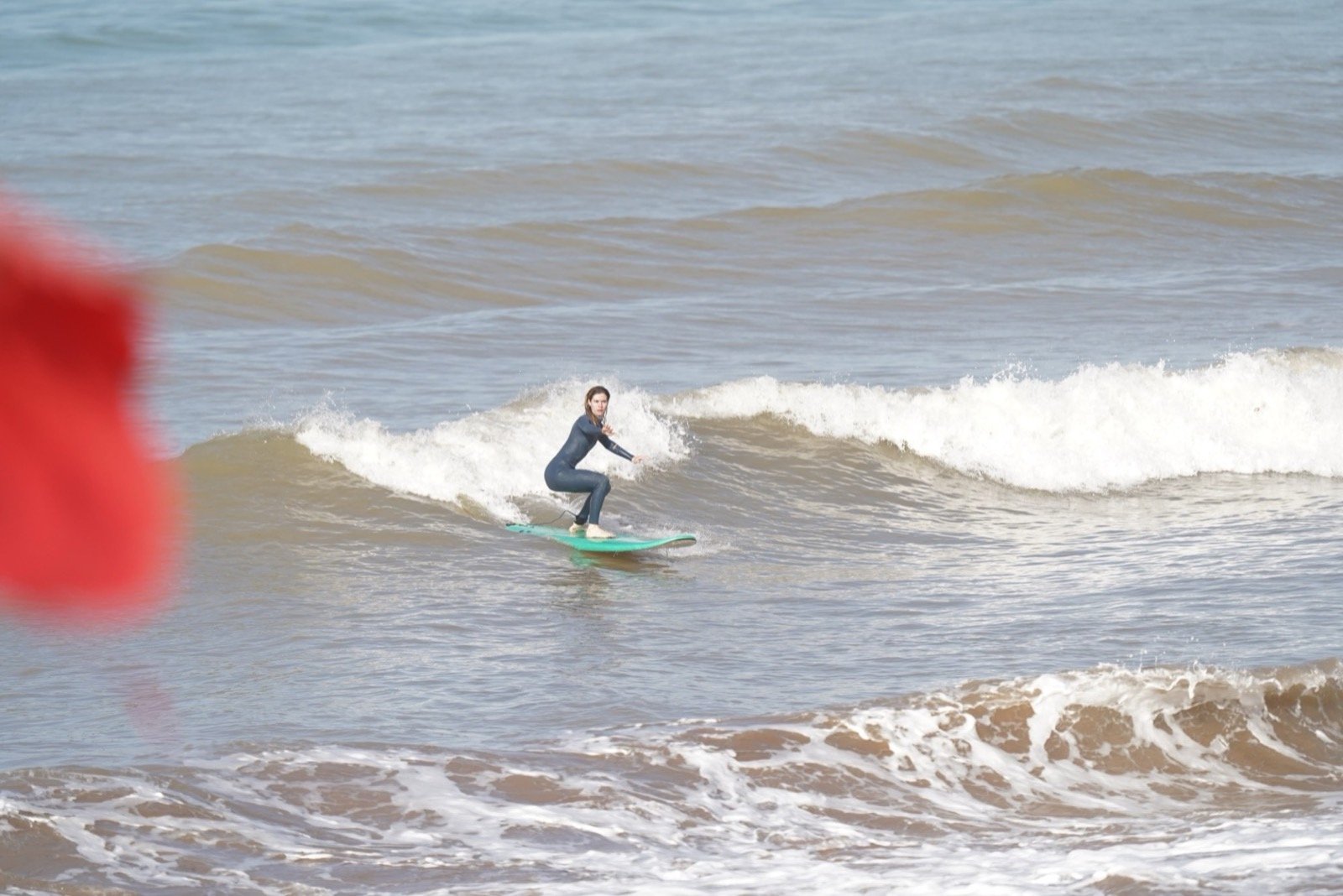 Alumno de surf surfeando una ola pequeña sobre una tabla verde en Taghazout