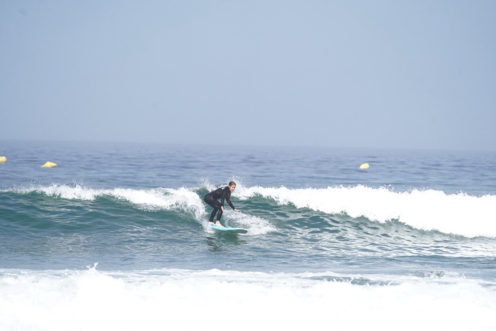 Alumna de surf surfeando una ola verde limpia sobre una tabla azul en Taghazout