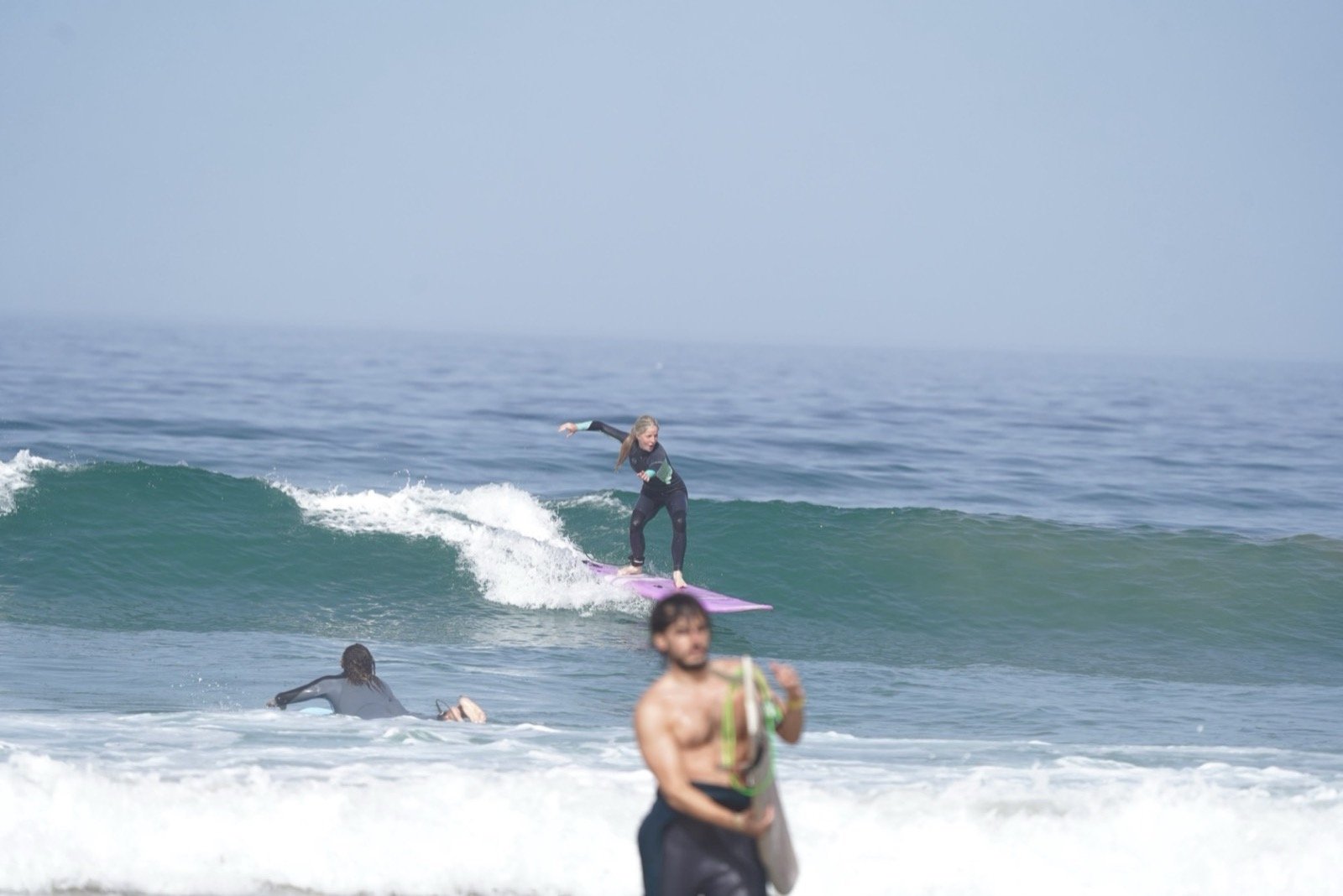 Alumno de surf surfeando una ola sobre una tabla morada durante una clase en Taghazout