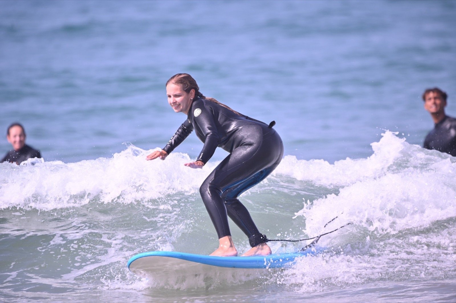 Alumno de surf de pie sobre una tabla azul en la espuma en Taghazout