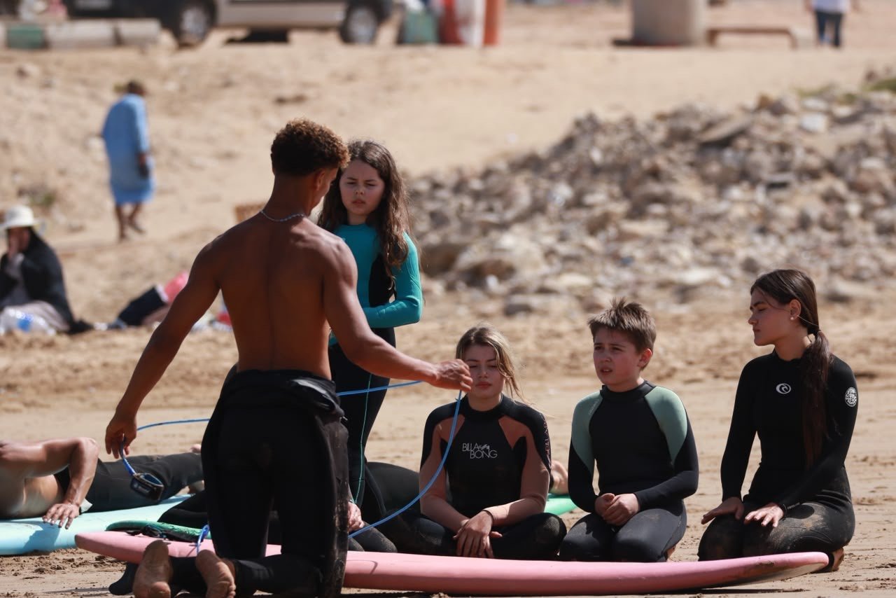 Coach explaining surf basics to students sitting on the sand