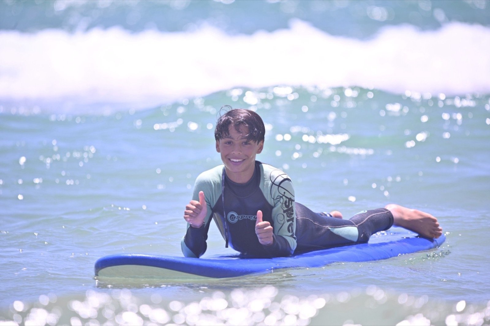 Joven surfista tumbado en una tabla en el agua levantando el pulgar durante una clase